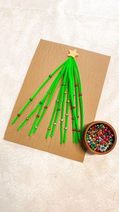 a christmas tree made out of green sticks and beads on a piece of brown paper