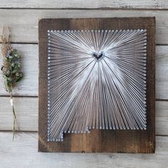 a string art piece is displayed on a wooden surface next to dried flowers and twigs