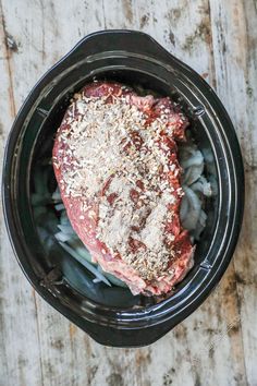 raw meat in a slow cooker with seasoning and salt on the top, ready to be cooked