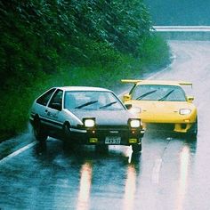 two cars driving down a wet road in the rain with trees and bushes behind them