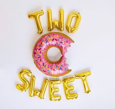 a donut with sprinkles and the word two sweet spelled out in gold balloons