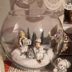 a glass bowl filled with snow and figurines on top of a table next to a teddy bear