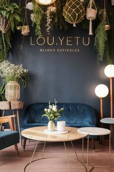 a living room with blue couches and plants on the wall behind it, in front of a sign that reads louuyetu