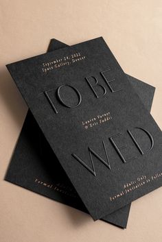 two black business cards with gold foil lettering on them, sitting on top of each other