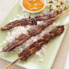 several skewers of meat and rice sit on a green plate with dipping sauce