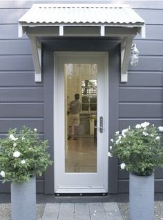 two planters with white flowers are in front of a gray building and the door is open