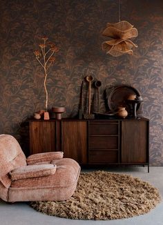 a living room with a chair and rug on the floor next to a dresser in front of a wallpapered wall