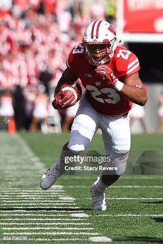 a football player is running with the ball in his hand and wearing a red uniform