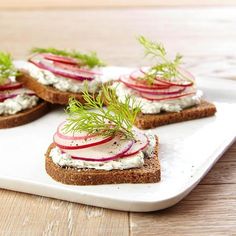 four slices of bread topped with cream cheese, radishes and dill sprigs