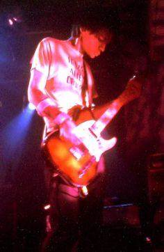 a man playing an electric guitar in front of some bright colored lights on the stage