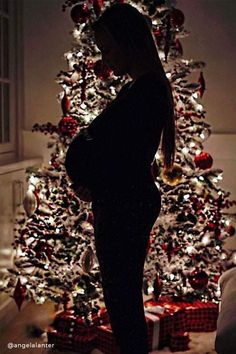 a pregnant woman standing in front of a christmas tree