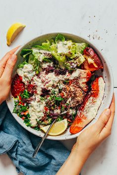 two hands holding a bowl of salad with lobster, lettuce and lemon wedges