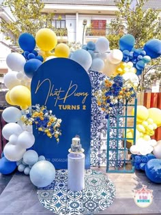 a blue and white backdrop with balloons, flowers and a sprayer on the ground