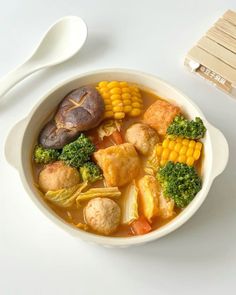 a bowl of soup with broccoli, corn and tofu on the side