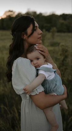 a woman holding a baby in her arms while standing in a field with tall grass