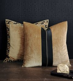 two black and gold pillows sitting on top of a wooden table next to each other