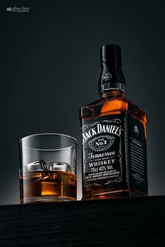 a bottle of jack daniels whiskey next to a glass with an ice cube in it