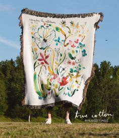 a woman is standing in the grass with a blanket on her back that has flowers and birds painted on it