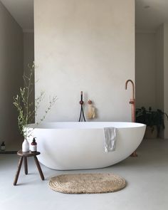 a large white bath tub sitting next to a wooden stool in a room with beige walls