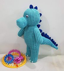 a blue knitted dinosaur next to a toy with gears in it's mouth