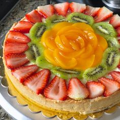 a cake with sliced kiwis, strawberries and oranges on it sitting on a plate