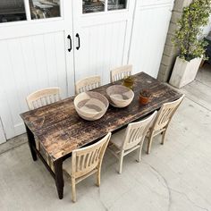 a wooden table with four chairs and two bowls on top of it in front of a white door