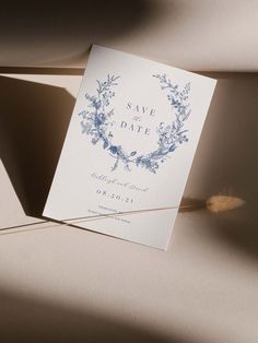 an elegant save the date card with blue flowers and leaves is displayed on a table