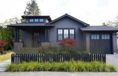 a gray house with lots of windows and plants on the front lawn in front of it