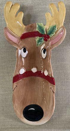 a ceramic reindeer mask with holly leaves on its antlers and nose is hanging from the wall