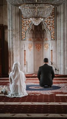 a man and woman sitting on the floor in front of a chandelier