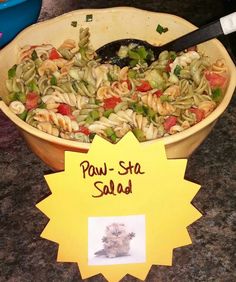 a bowl filled with pasta and vegetables next to a yellow sign that says paw - sta salad