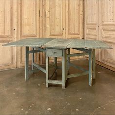 an old table with two smaller tables underneath it in front of wood paneled walls