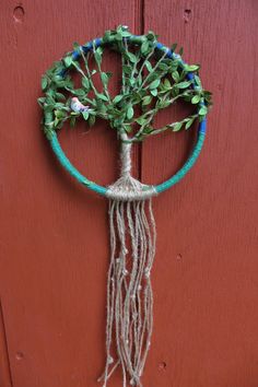 a tree made out of yarn hanging on a red door with green leaves and blue beads