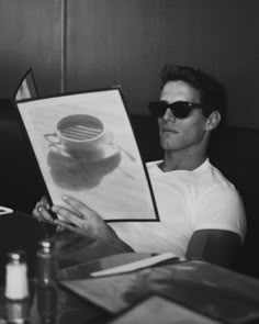 a man sitting at a table with a coffee cup in front of him holding up a drawing