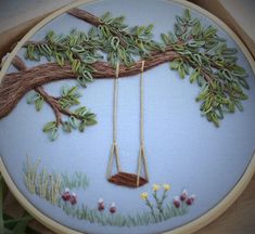 a hand embroidered wall hanging with a swing and tree branch in the middle, on a blue background