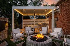 a fire pit sitting in the middle of a yard next to a patio with chairs and an umbrella