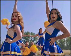 two women in cheerleader outfits are holding up yellow pom - poms while others look on