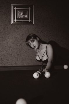 a woman is playing pool with balls on the table in front of her and looking at the camera