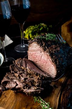 a large piece of meat sitting on top of a wooden cutting board next to two glasses of wine