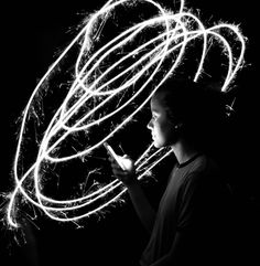 a woman holding a cell phone in her hand while she is lit up with sparklers