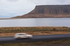 a white car driving down the road near a large body of water with a mountain in the background