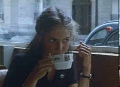 a woman sitting at a table drinking from a cup