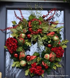 a christmas wreath with red and green decorations on the front door, decorated with greenery