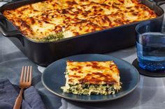 a casserole dish with cheese and spinach is on a plate next to a glass of water