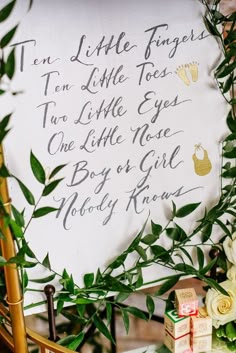 a white sign with writing on it next to flowers and greenery in front of a wooden chair