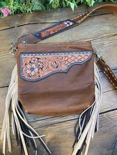 Handmade Brown leather purse with cream and dark  brown fringe. The front has  a hand tooled floral leather patch with cream color accents and buck stitch Measures 10 1/2 x 10 Zipper closure with fun farm print lining. Inside has card slot pockets and a zipper pocket. There is one large zipper pocket on the outside (perfect for a cell phone) Long adjustable cross body strap fully buck stitched with antique silver and copper floral design buckle. 46-50" Leather Bags With Concho For Everyday Use, Western Style Hand Tooled Brown Shoulder Bag, Western Style Brown Hand Tooled Shoulder Bag, Western Leather Bags With Concho Details, Hand-tooled Leather Bags For Western-themed Events, Leather Hand Tooled Shoulder Bag For Western-themed Events, Hand Tooled Leather Bags For Western-themed Events, Bohemian Brown Bags With Concho, Western-themed Brown Leather Shoulder Bag