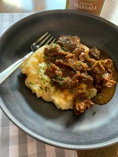 a plate with mashed potatoes, meat and gravy on it next to a bottle of wine