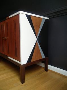 a wooden cabinet sitting on top of a hard wood floor next to a black wall