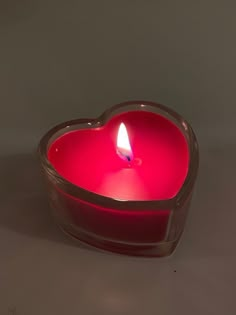 a heart shaped candle with a lit candle inside on a gray surface, in the shape of a heart