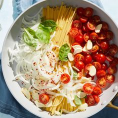 a white bowl filled with pasta, tomatoes and other vegetables on top of a blue towel